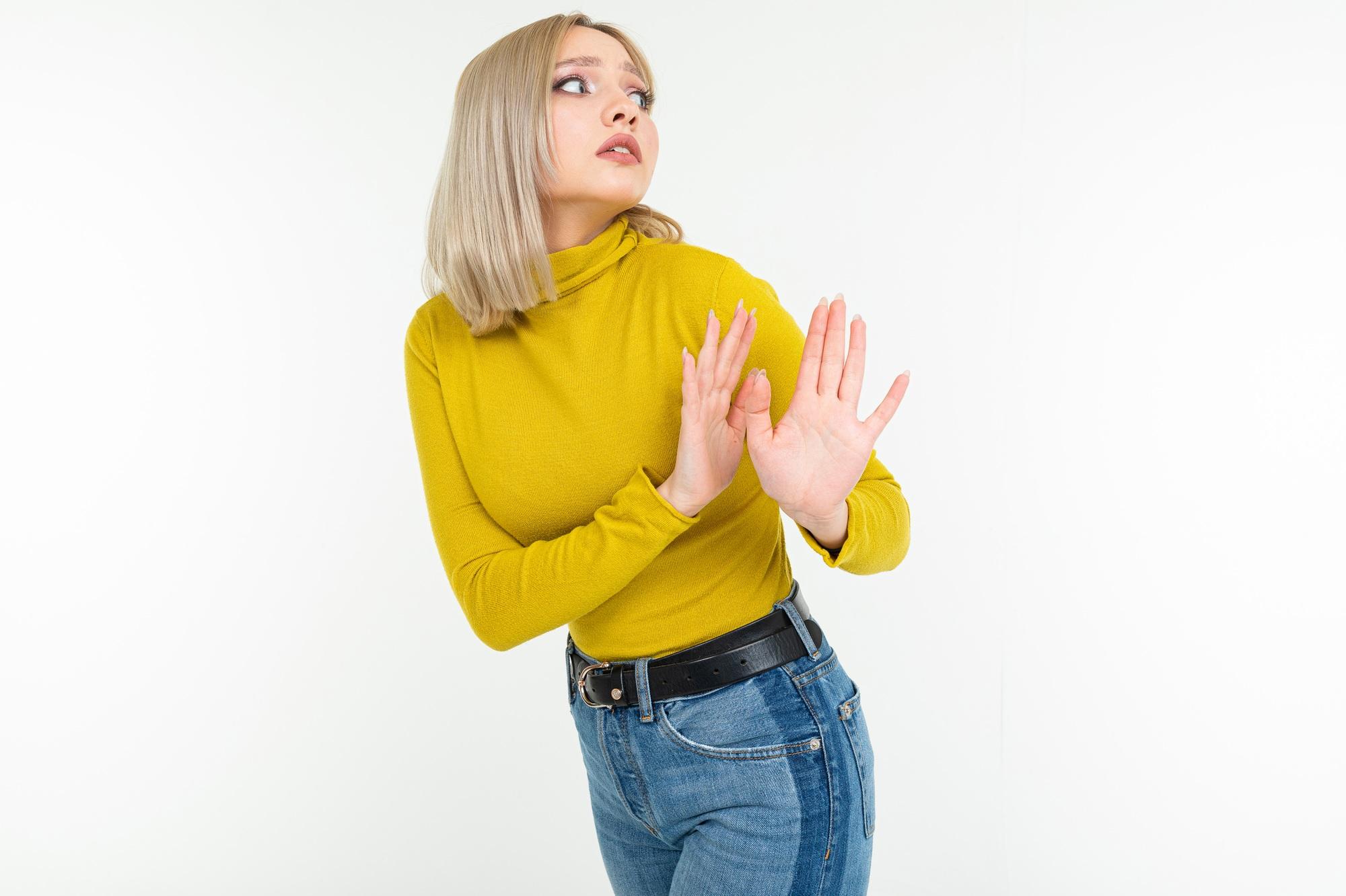 sexy blonde lady in tight lemon blouse and jeans warns with her hands on a white background